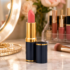 Coral pink lipstick tube with navy cap and gold accents, standing on vanity