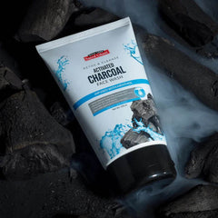 Activated charcoal face wash tube on dark charcoal chunks, blue accents, 100 ml
